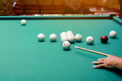 Playing billiards, close up of a mans hand with a cue hitting a white ball. balls with numbers 