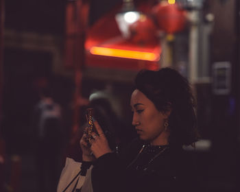 Portrait of young woman holding camera at night