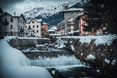 Snow covered buildings by houses in city during winter