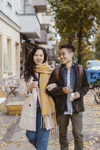 Male and female friend talking while strolling on sidewalk during autumn