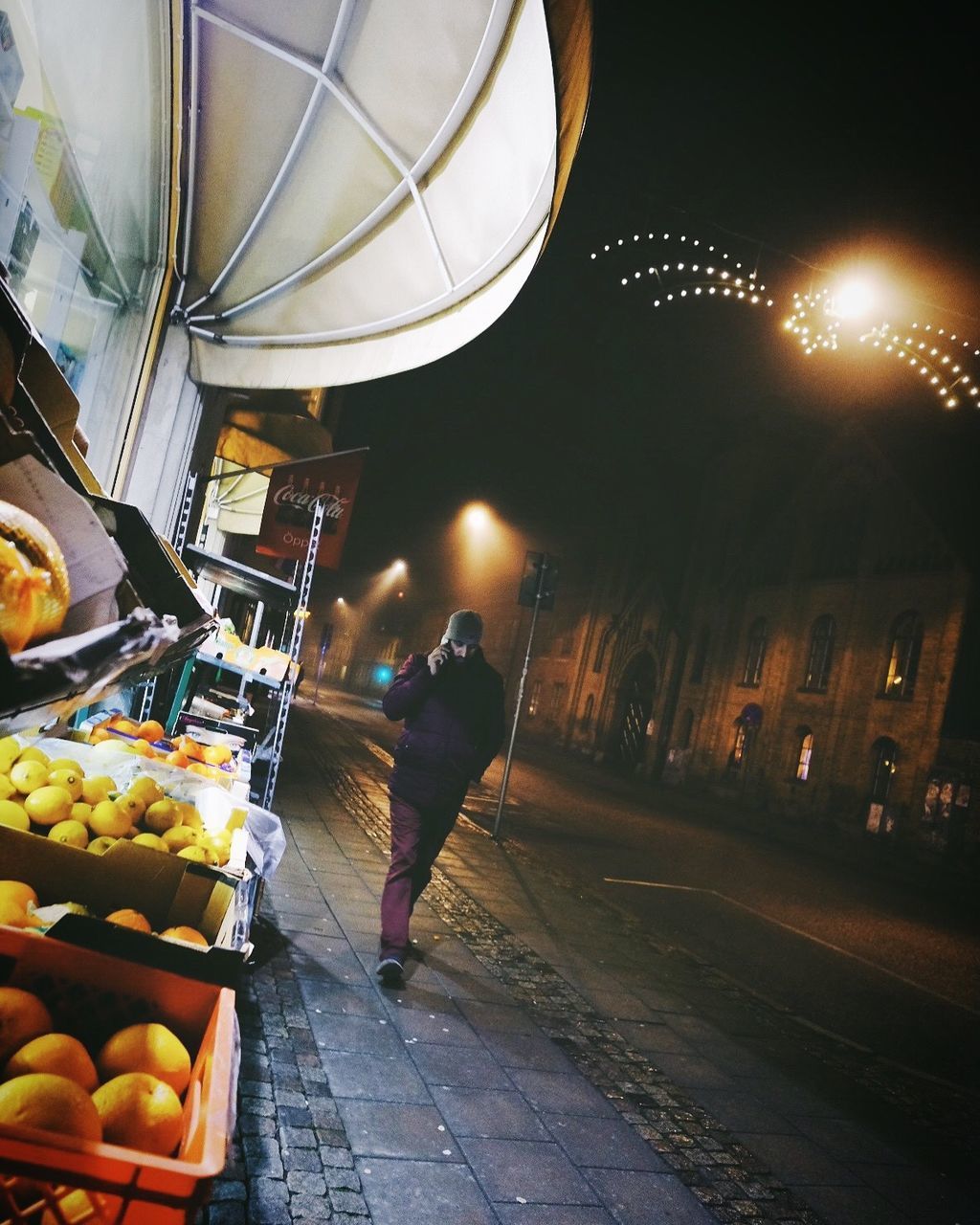 REAR VIEW OF MAN WALKING ON ILLUMINATED STREET MARKET AT NIGHT