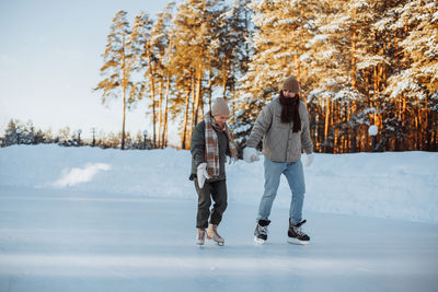 A couple in love skates holding hands on a skating rink outdoors in the park in winter