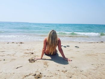 Rear view of young woman reclining on sand at beach during sunny day