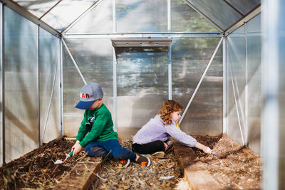 Young kids using shovels to clean out greenhouse in backyard