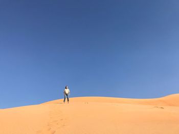 Man walking in desert against clear blue sky