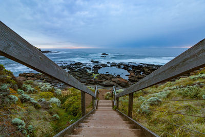 Footpath leading towards sea against sky