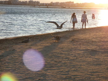 People at beach against sky during sunset