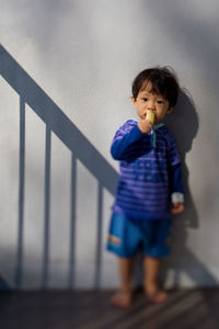 Portrait of cute boy eating banana while standing against wall