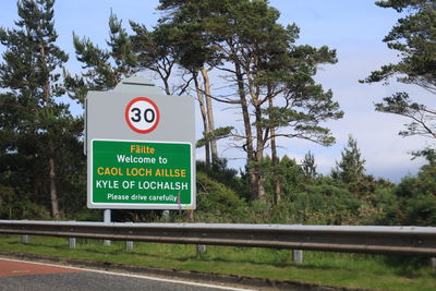 Road sign by trees against sky