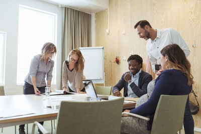 Male and female business professionals discussing over documents at meeting