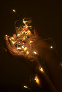 Close-up of cropped hands holding illuminated christmas lights