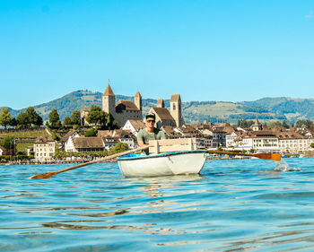 Man oaring boat on river against clear blue sky