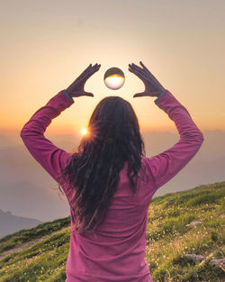 Rear view of woman standing against sky during sunset