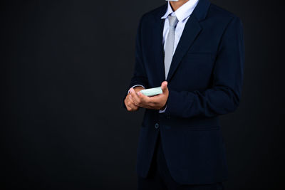Midsection of man holding camera while standing against black background