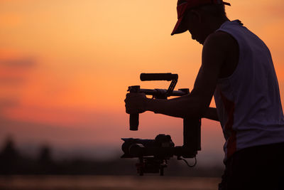 Silhouette man photographing working against sky during sunset