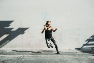 Dedicated female athlete exercising on sidewalk against white wall