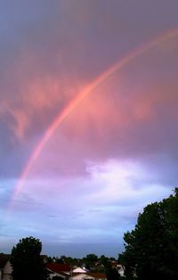 Rainbow over trees against cloudy sky