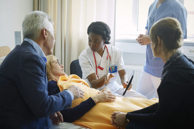 Doctor with nurse explaining mature patient and her friends at hospital ward