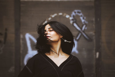 Portrait of beautiful young woman standing against wall