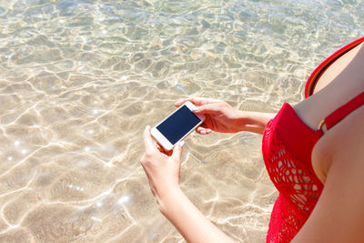 Midsection of woman photographing sea while standing at beach