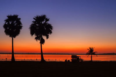 Silhouette palm trees on beach against sky during sunset