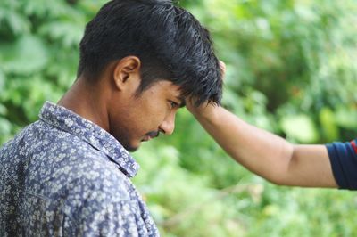 Cropped hand of person touching friend head against trees