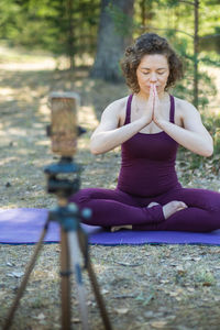 Young woman doing yoga in nature online using phone and application