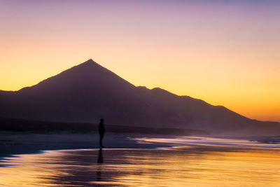 Silhouette person in sea against sky during sunset