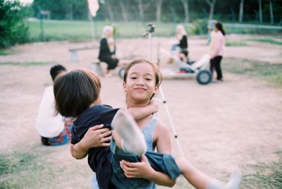 Portrait of smiling girl carrying sibling while walking in playground