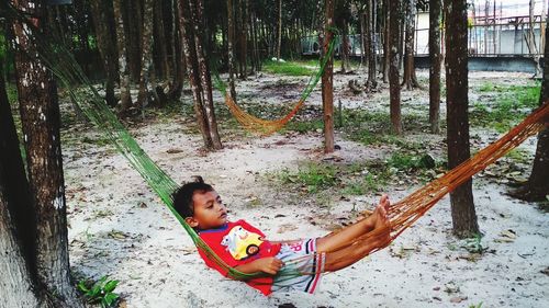 Full length of cute boy on tree trunk in forest