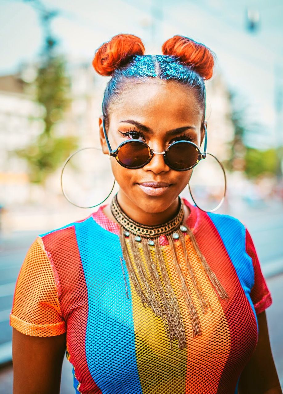 portrait, glasses, focus on foreground, front view, one person, young adult, fashion, smiling, looking at camera, sunglasses, standing, jewelry, day, lifestyles, real people, multi colored, emotion, happiness, leisure activity, outdoors, hairstyle, beautiful woman