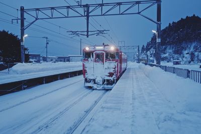 Train on snow covered railroad tracks against sky during winter