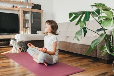 The girl sits in the lotus position and meditates at home in the living room. yoga poses for kids