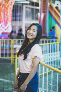 Portrait of smiling young woman standing against railing