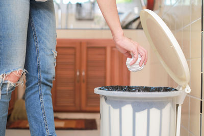 Midsection of woman putting garbage in bin at home