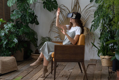 Young woman wearing vr helmet experiencing virtual reality while resting in greenhouse