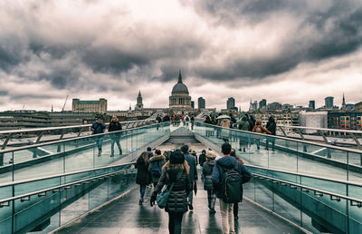 Rear view of people on bridge in city against sky