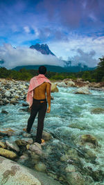 Rear view of man standing on rock against sky