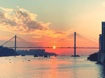 Suspension bridge over sea against sky during sunset