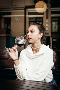 Young woman looking away while sitting in glass