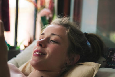 Beautiful young woman reading a book at home while lying on sofa