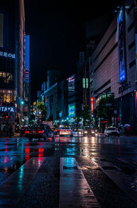 Wet illuminated city street against sky at night