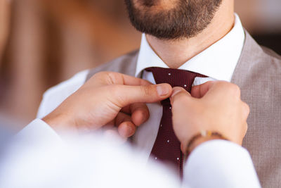 Cropped hands of man adjusting bridegroom necktie at wedding