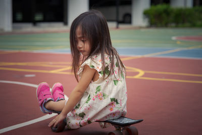 Rear view of cute girl playing with skateboard outdoors