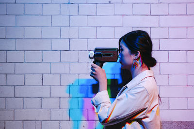 Woman filming through video camera in front of wall