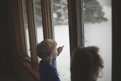 Siblings looking through window while standing at home