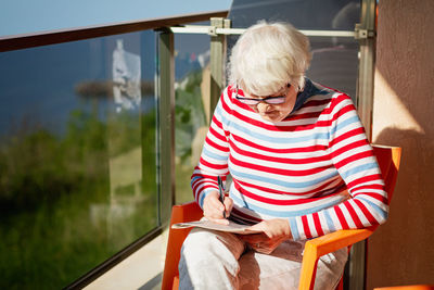 Senior woman in glasses sitting on balcony near the sea