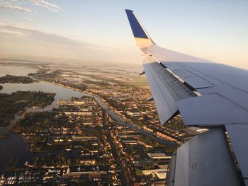 Cropped image of airplane wing flying over city during sunset