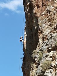 Low angle view of man climbing on rock against sky