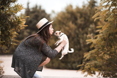 Woman wearing hat embracing dog at park